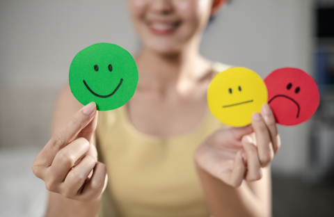 Woman holding two cutouts showing happy and sad faces showing emotional regulation